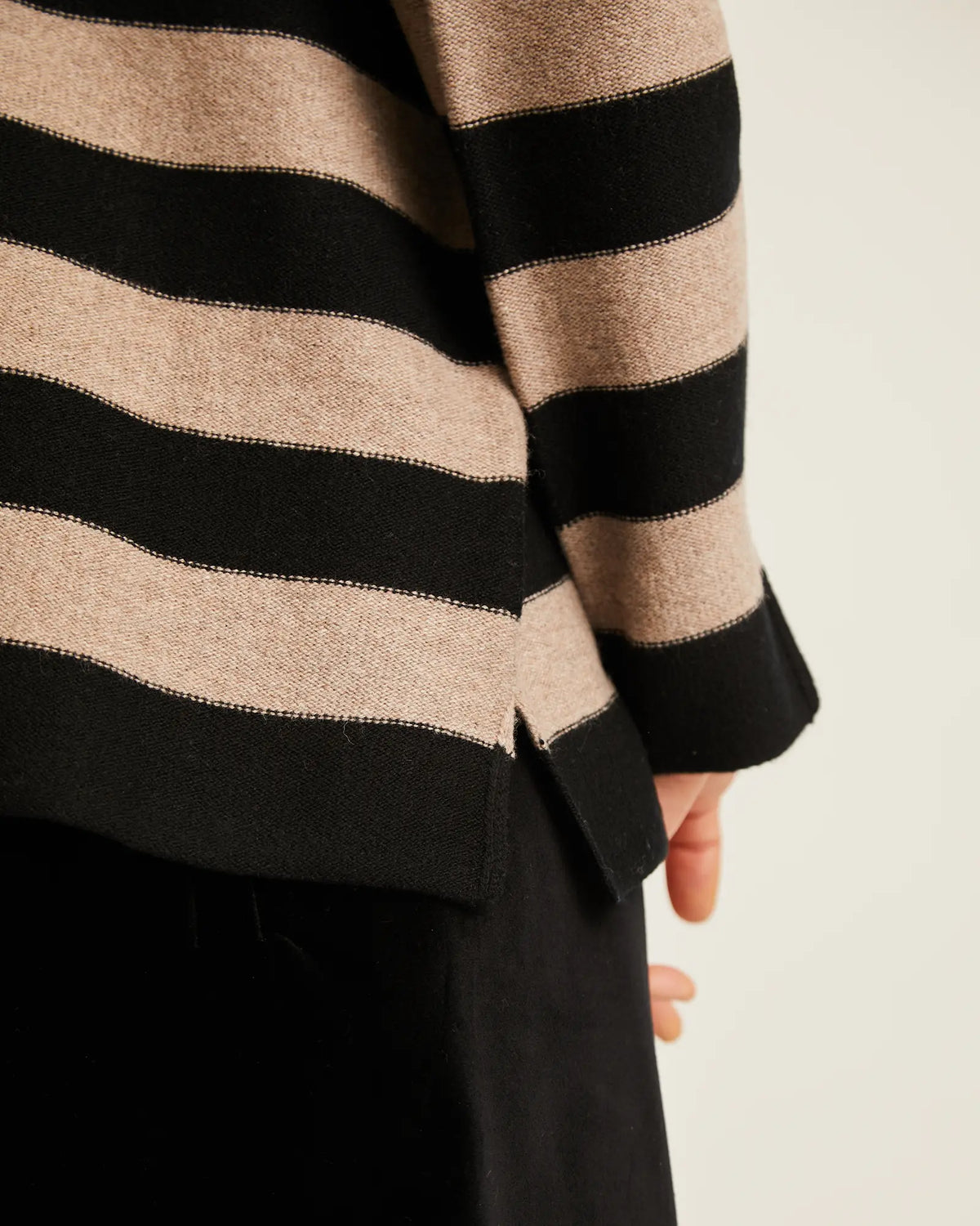 Close-up of a striped knit sweater with wide beige and black horizontal stripes, worn by a model against a plain light background.