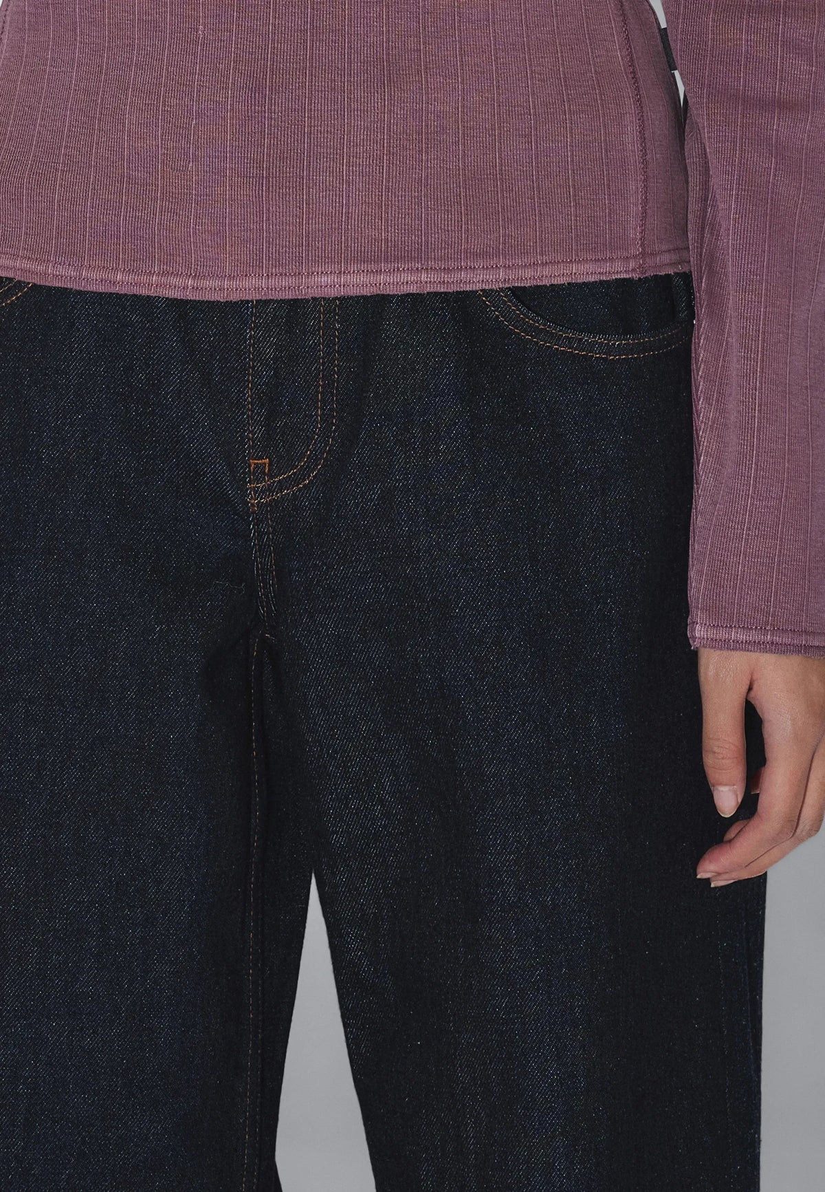 Person wearing a purple shirt and dark jeans on a plain background