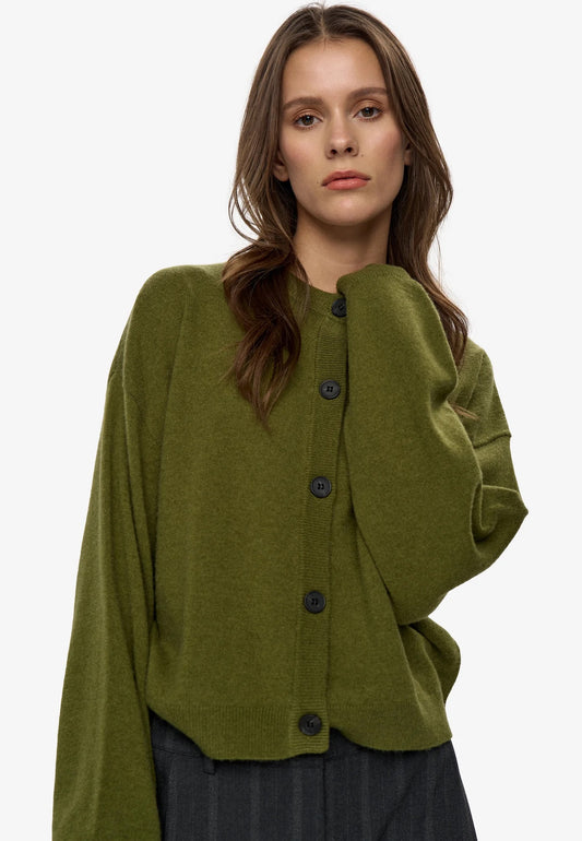 A woman wearing a cropped, olive green knit cardigan with dark buttons, photographed against a clean white studio background.