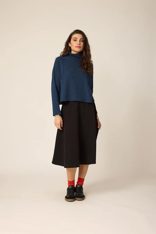 Woman wearing a blue top and black skirt on a beige background