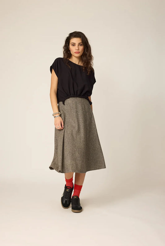 Woman wearing a black top and gray skirt on a beige background
