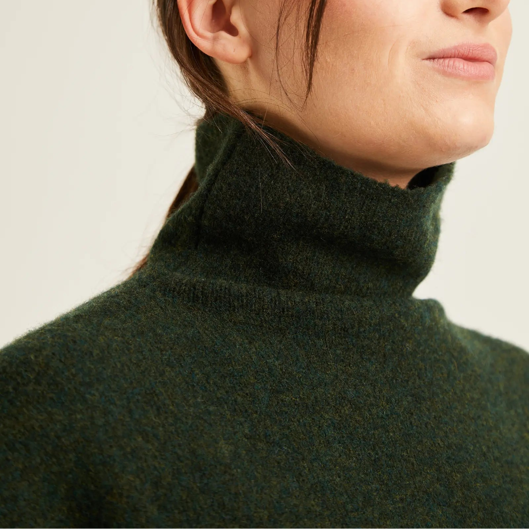 Close-up of a woman wearing a dark green high-neck knit sweater against a plain light background.