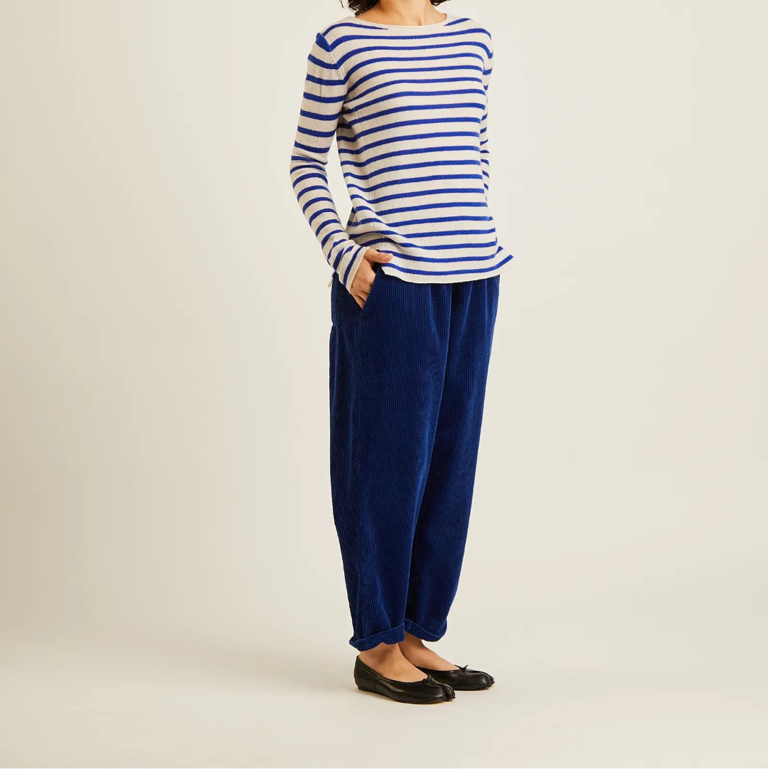 A model wearing a blue and white striped long-sleeve top, navy blue velvet wide-leg pants, and black flat shoes, standing against a plain light beige studio background.