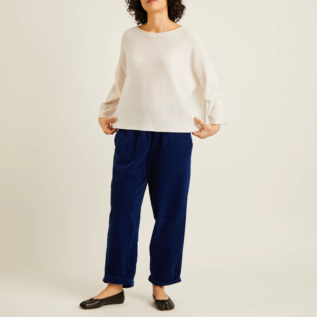 A model wearing a cream-colored knit long-sleeve top and navy blue wide-leg trousers, paired with black flats, against a plain light beige studio background.