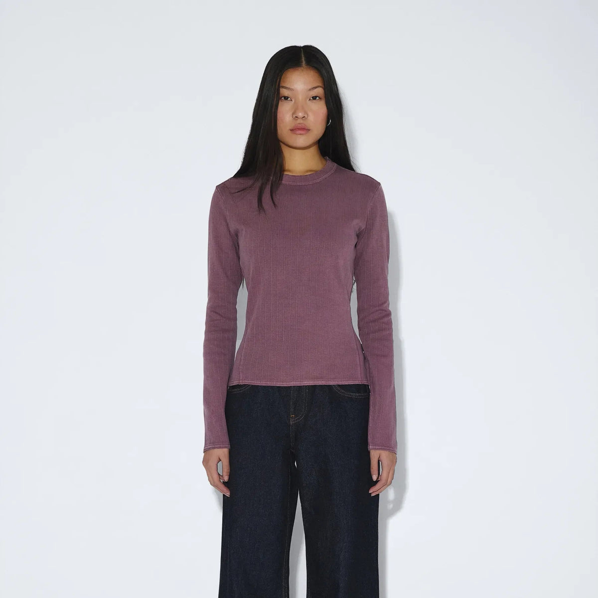 Person wearing a mauve long-sleeve top and black wide-leg pants on a white background