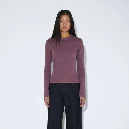 Person wearing a mauve long-sleeve top and black wide-leg pants on a white background