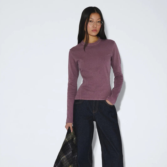 Woman wearing a purple top and dark pants holding a plaid coat on a white background