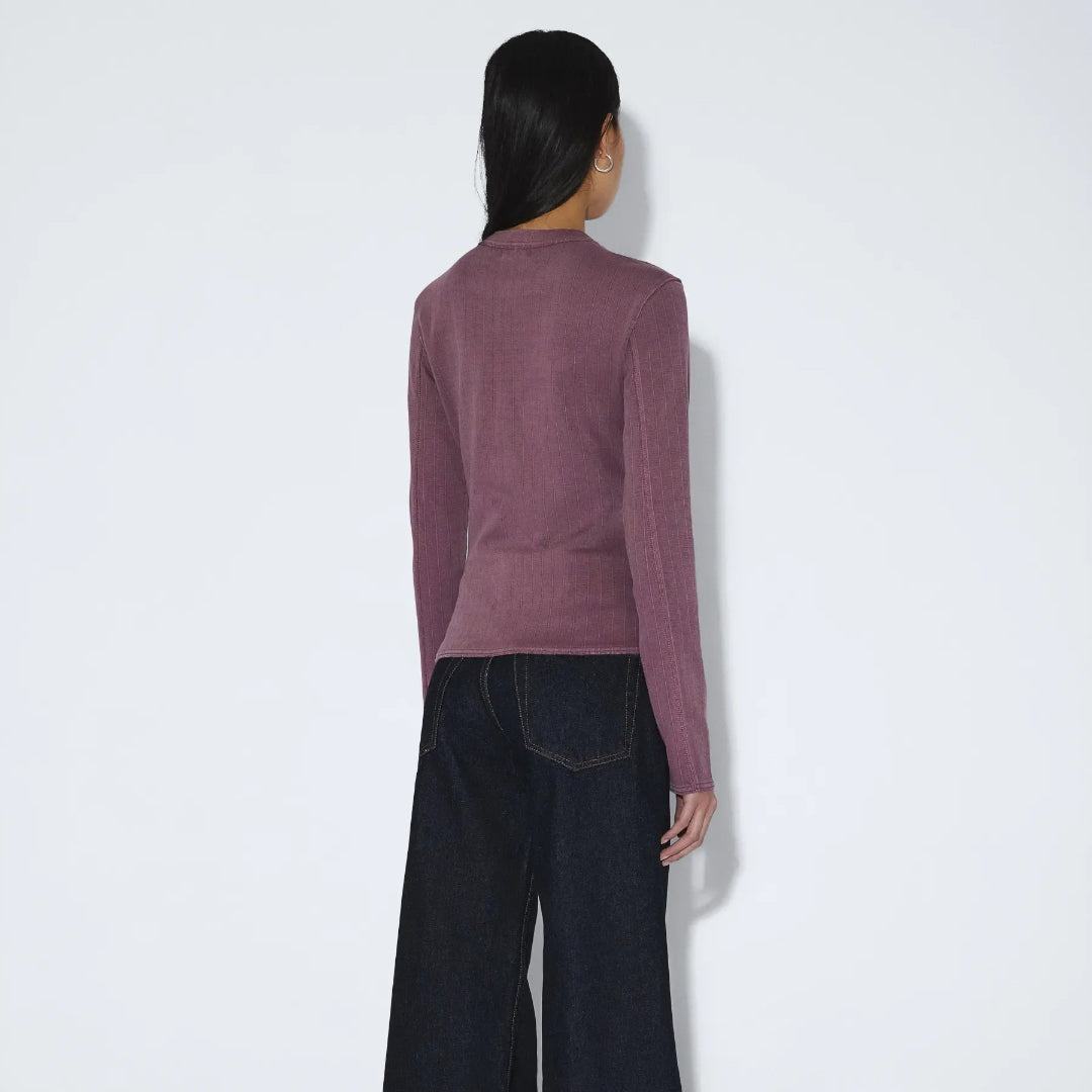Person wearing a mauve sweater and dark pants on a white background