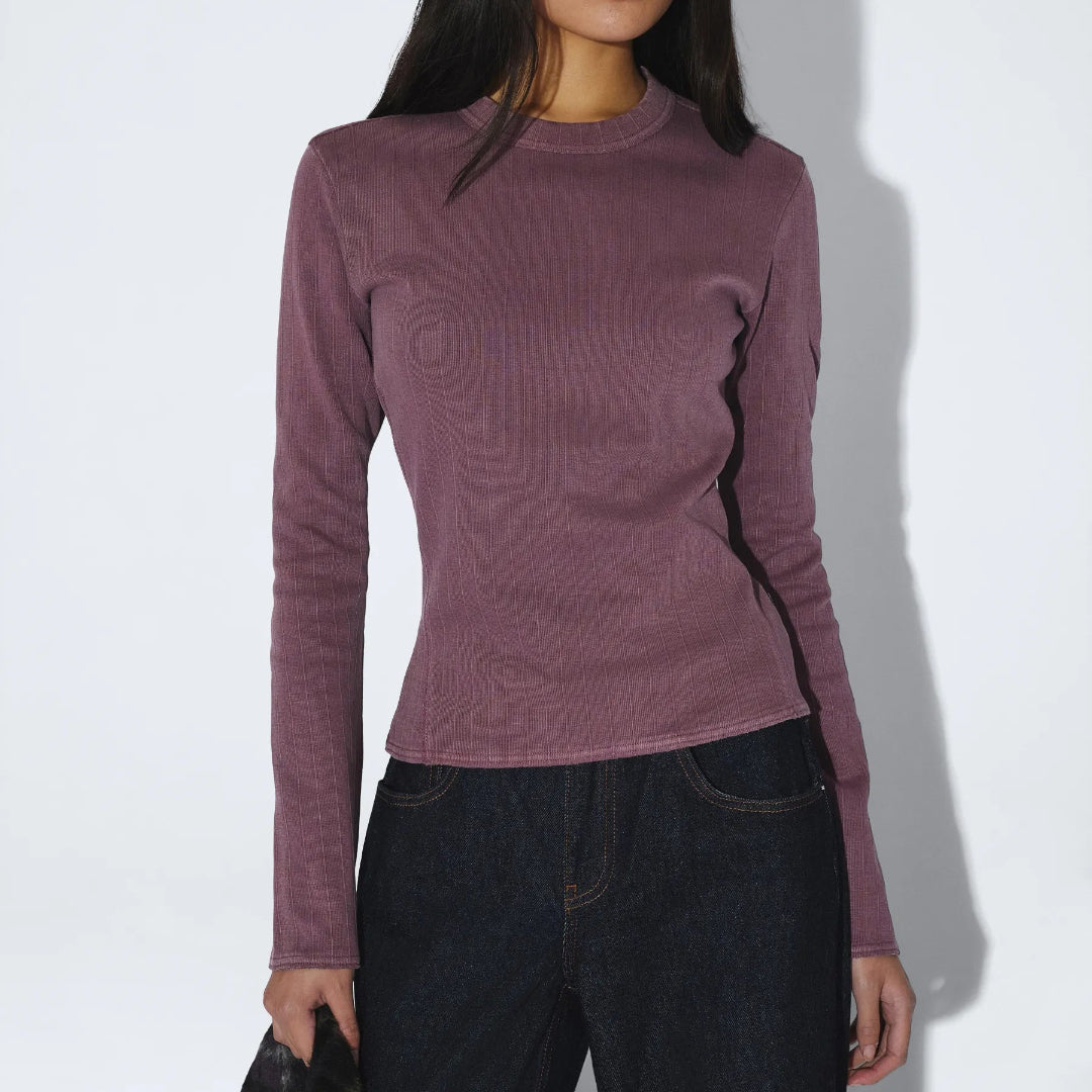 Person wearing a purple long-sleeve top and dark pants against a white background