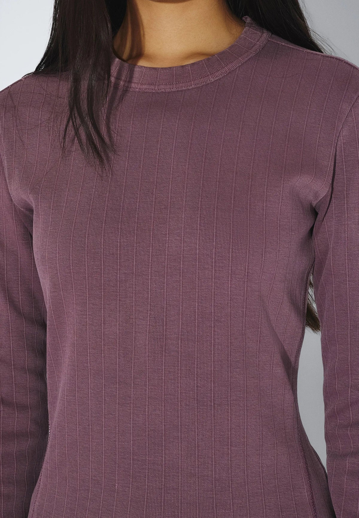 Close-up of a person wearing a textured purple long-sleeve shirt against a neutral background