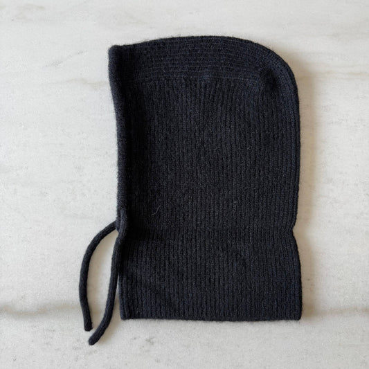 A black ribbed knit pouch with a drawstring, laid flat on a light gray marble surface.