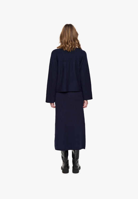 Woman from behind, wearing a navy blue sweater and knit midi skirt on a white background