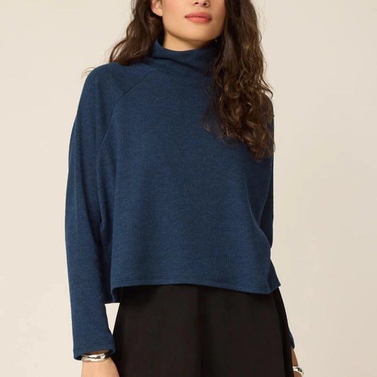 Woman wearing a blue turtleneck sweater against a beige background