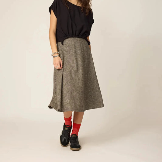 Woman wearing a black top and gray skirt on a beige background
